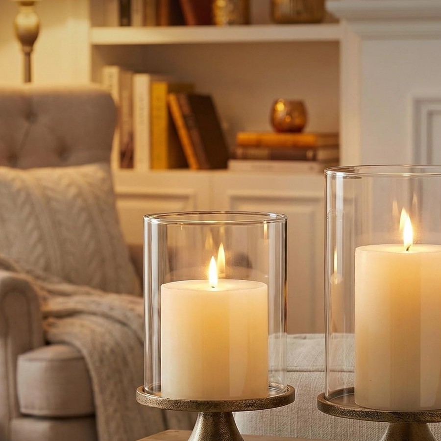 Two pillar candles under glass domes beside a lit fireplace